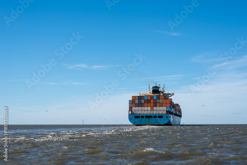 A large container ship seen from behind, with many seagulls near the ship.