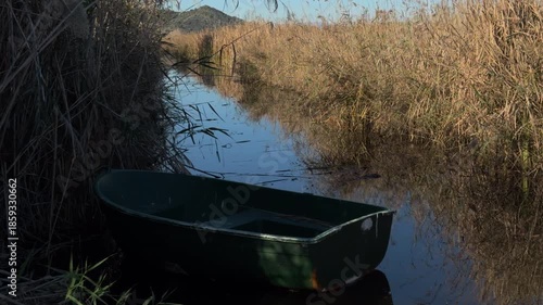 Still green boat in golden reed canal at sunset