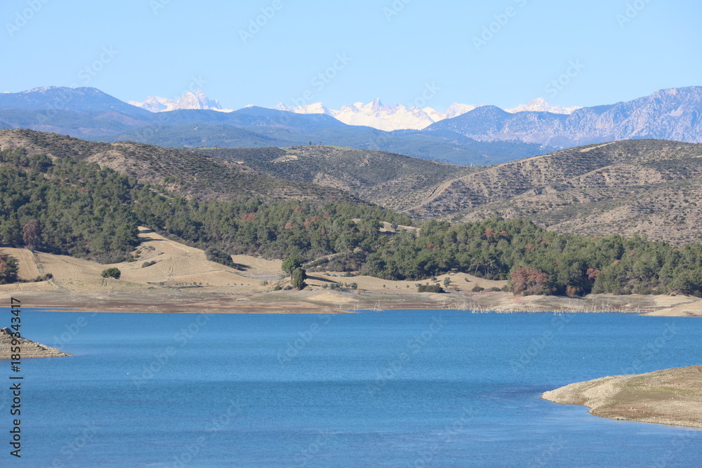 Fototapeta premium Breathtaking panoramic view of a deep blue lake surrounded by pine forests and snowy mountain peaks