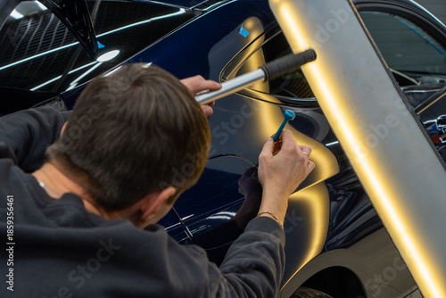 Process of paintless dent repair on car body. The mechanic at the auto shop with tools to repair dents in car body. Body repair. A specialist repairs a dent on the car body without painting. PDR. 