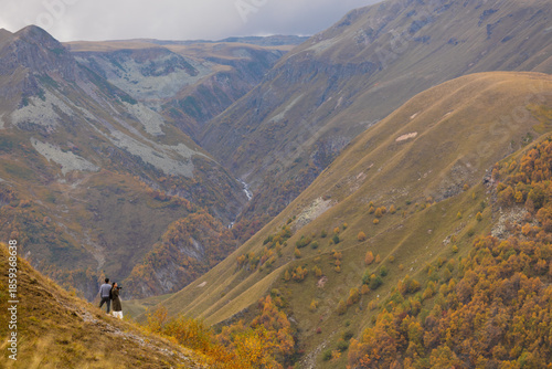 Couple Standing On Steep Cliff Edge Overlooking Autumn Mountain Canyon