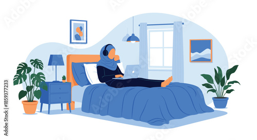 Young muslim woman wearing blue hijab sitting on bed with laptop and headphones studying or working in cozy bedroom interior.