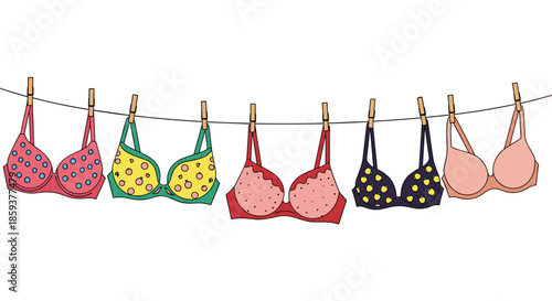 Row of colorful bras with various patterns like polka dots and apples hanging from a laundry line with wooden clothespins.