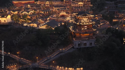Aerial view of illuminated traditional buildings and pathways in Wangxian Valley, creating a warm glow against the night, Wangxian Valley, China.