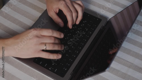 Top view close up of male hands typing on a laptop keyboard on a table. Natural hand position, steady working rhythm, calm indoor light and focused everyday computer activity. High quality 4k footage