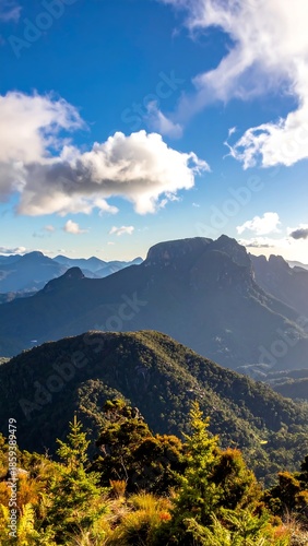 Mountainous landscape featuring sunny skies with patchy clouds casting shadows over lush green peaks and valleys