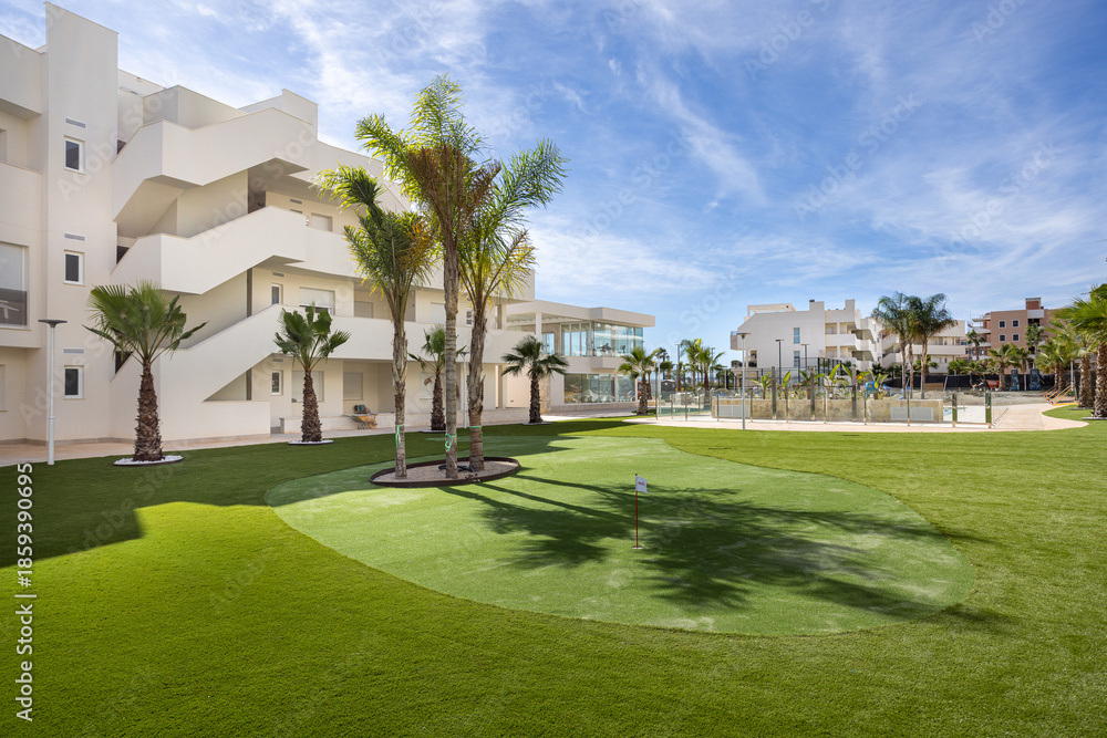 Fototapeta premium Modern residential complex with palm trees and putting green under blue sky