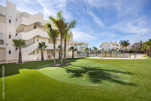 Modern residential complex with palm trees and putting green under blue sky
