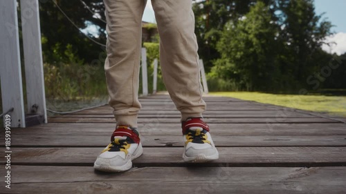 Front view of boys sneakers as he stands still on wooden pier. Scene emphasizes balance, calmness and healthy outdoor lifestyle. High quality 4k footage