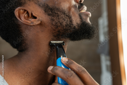Foto Close-up of a Black man trimming his beard with an electric shaver in a bright bathroom