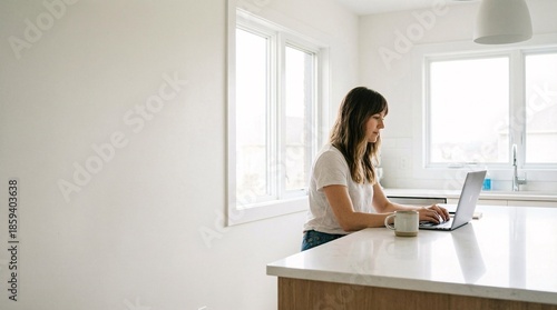 Woman working remotely on laptop in modern kitchen with coffee