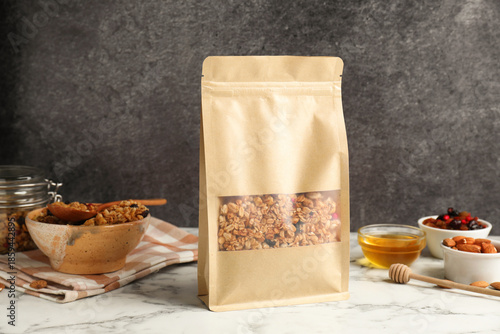 Schilderij op canvas Paper bag with tasty granola on white marble table, closeup