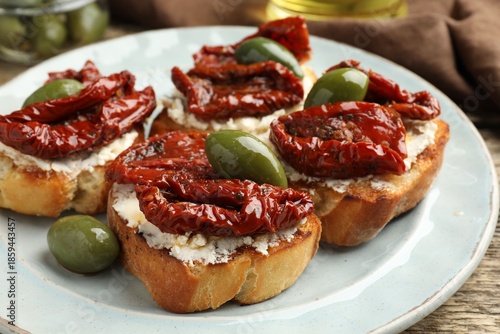 Delicious bruschettas with cream cheese, sun-dried tomatoes and green olives on table, closeup
