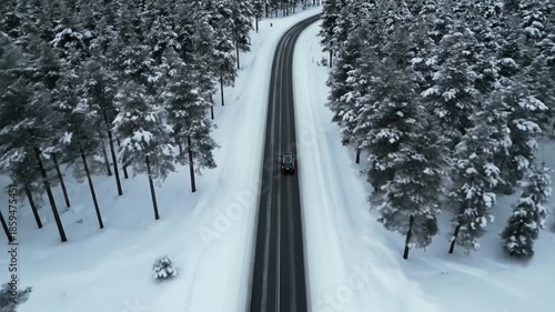 Aerial view of a black car traveling on a paved road surrounded by snow-covered pine trees. Captures a serene winter journey atmosphere, ideal for travel vlogs and nature documentaries.