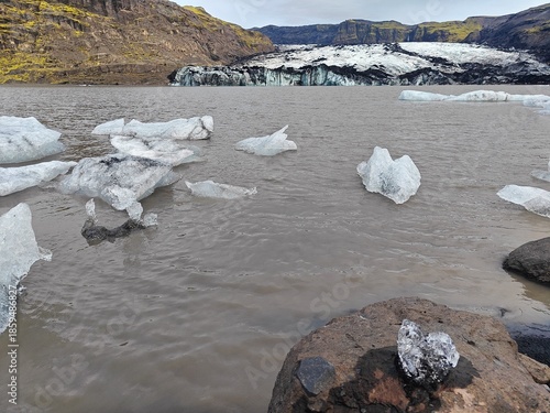 Glacial lagoon with floating icebergs and Sólheimajökull glacier tongue in Iceland. Stunning Nordic volcanic landscape under overcast sky.