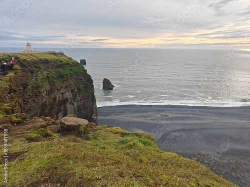 Scenic view from a cliff of a black sand beach and Dyrhólaey lighthouse in Iceland. Dramatic coastal landscape with volcanic sand.
