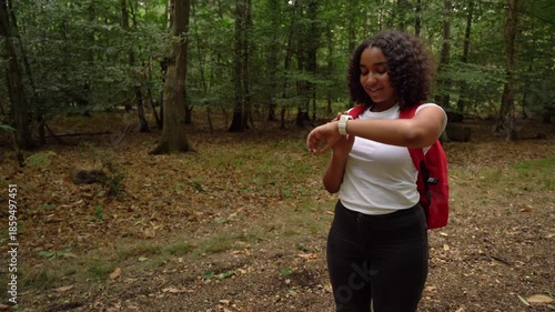 Teenage mixed race African American girl young woman hiking with a red backpack and wearing a smart watch in forest woodland 
