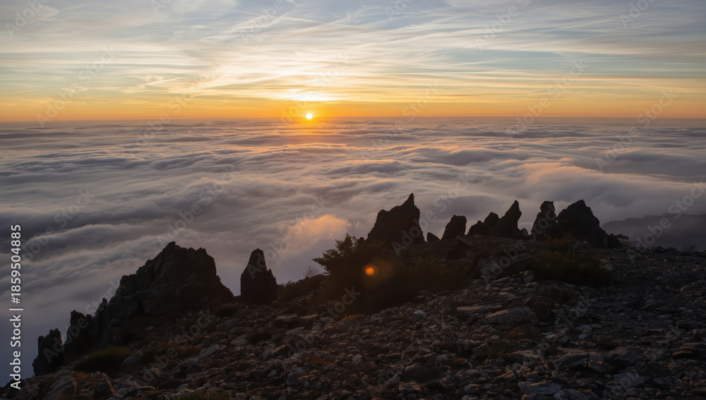 Fototapeta premium Sunrise above layered cloud sea with jagged mountain ridge and warm light