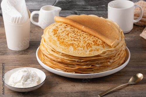 Stack of golden crepes served with sour cream on a wooden table