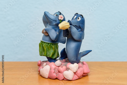 A collectible figurine set featuring two blue dolphins in whimsical, romantic attire, possibly a cake topper or miniature decor. 