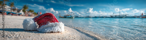Vibrant red Santa hat resting on sun-kissed white sand beach next to serene ocean waves