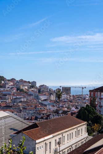 A classic wrought iron fence and street lamp at a Lisbon miradouro, framing the city and the Tagus river in the distance.