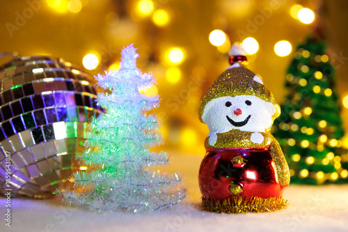 White and green Christmas trees with a snowman and a Christmas ball on a blurred background with yellow lights