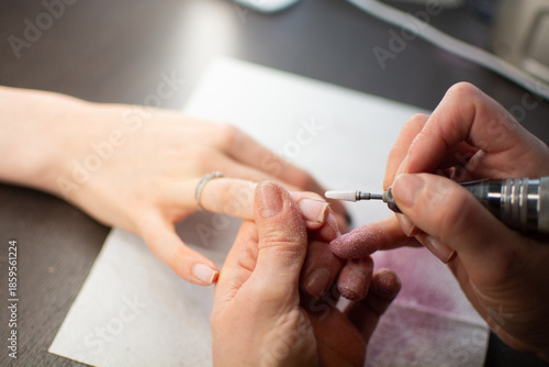 A nail technician removes gel polish from a clients nails using an electric nail drill