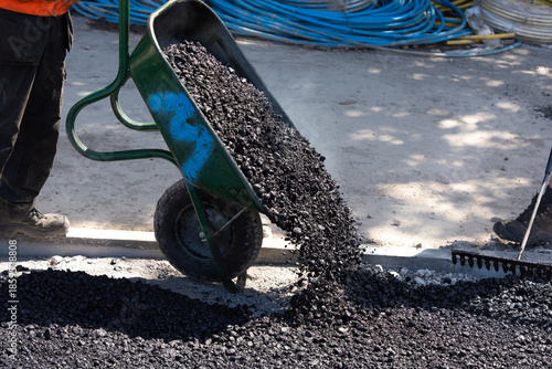 Fotografie Construction workers in high-visibility gear are applyin gfresh hot asphalt to r