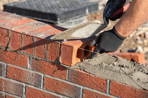 Bild auf Leinwand Close-up of skilled bricklayer working on construction site laying red bricks fo