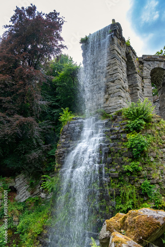 Tranquil Waterfall With Lush Surroundings, Serene Waterfall Flowing Beneath Stone Bridge Amidst Vibrant Woods
