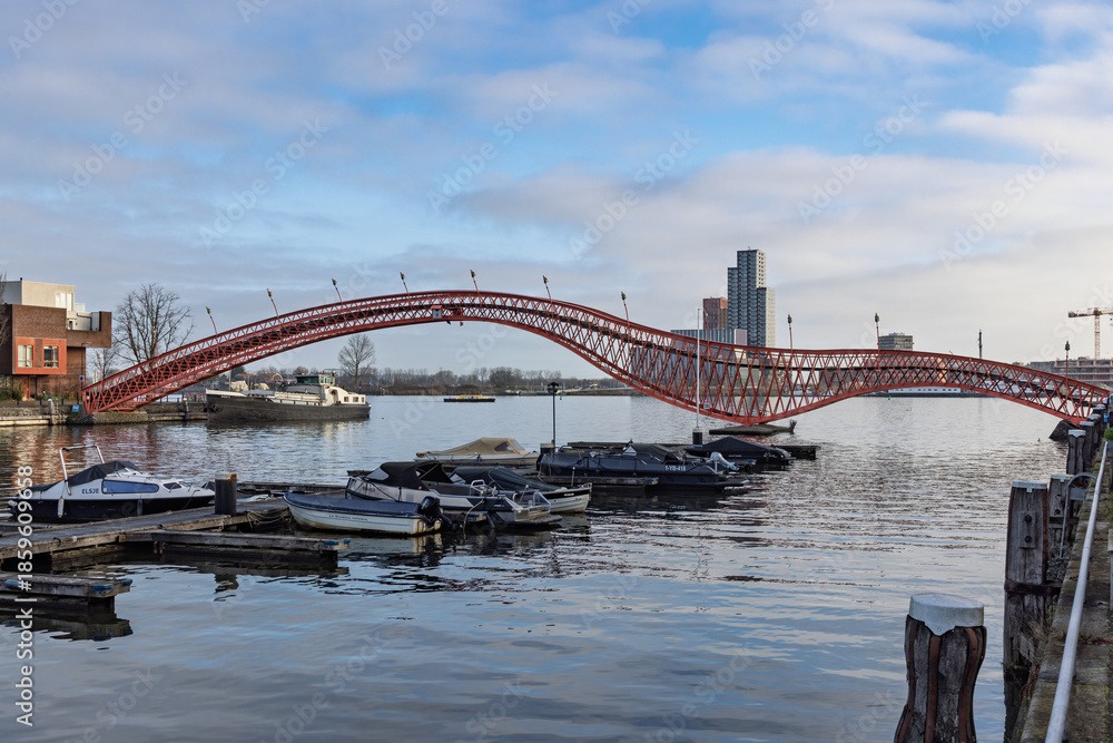 Fototapeta premium The iconic red Python Bridge (Pythonbrug) spanning the canal in Amsterdam's Eastern Docklands, connecting Sporenburg and Borneo Island.