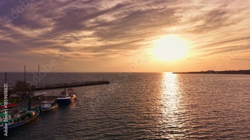 Warm golden rays stretch across the horizon as boats gently sway in the harbor, creating a tranquil scene filled with peace and natural beauty at sunset.