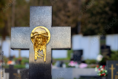 Black cross with golden statue in cemetery at sunset with burning candle. Memory of deceased. Expression of love.