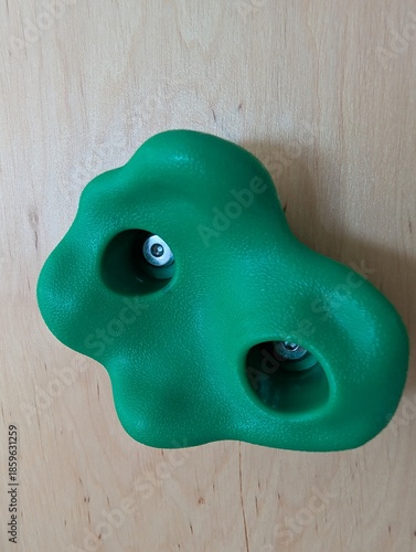 Green plastic climbing wall hold isolated on wooden surface, indoor sport and fitness equipment.