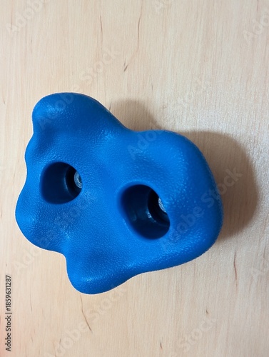 Blue plastic climbing wall hold isolated on wooden surface, indoor sport and fitness equipment.