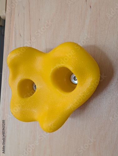 Yellow plastic climbing wall hold isolated on wooden background, indoor climbing equipment detail.