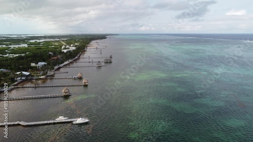 Aerial Drone View of Caye Caulker Island with Mangroves and Turquoise Sea, Belize.  Aerial drone shot of Caye Caulker Island in Belize, showcasing lush green mangroves, coastal houses, sandy paths.
