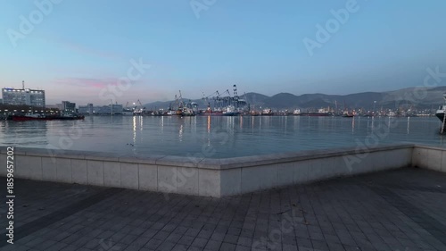 Wallpaper Mural A tiled embankment in a port city on the Black Sea. A walk through Novorossiysk. Evening landscape. Sunset. The sea, mountains, ships, loading equipment, wild birds, and calm water Torontodigital.ca