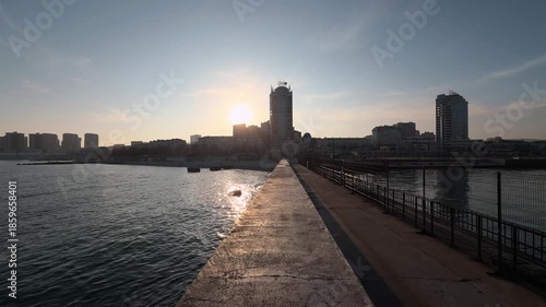 Wallpaper Mural A walk along the pier by the sea in Novorossiysk bay. Calm sea surface, ripples on the water. City view in the background. Wide angle. Sunset. Against the sun. Atmospheric B-roll 3 Torontodigital.ca
