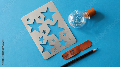 Artistic Still Life Composition Featuring a Star Stencil, Glass Bottle with Constellation Design, Leather Strap, and Pencil on a Vibrant Blue Surface for Creative Projects
