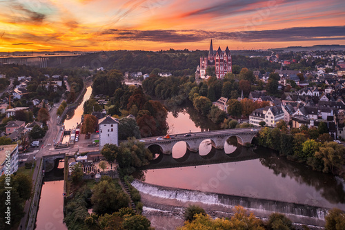 Aerial view of the serene Lahn river reflecting the vibrant sunset sky, with the majestic Limburger Dom standing tall, Limburg an der Lahn, Hessen, Germany.