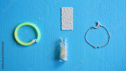 Artistic Still Life Composition Featuring a Neon Bracelet, Textured Tile, Small Bottle with Stones, and Crescent Bracelet on a Vibrant Blue Background, Showcasing Contrasting Textures