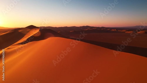 Desert landscape at sunset featuring sand dunes with warm orange and red colors a clear sky