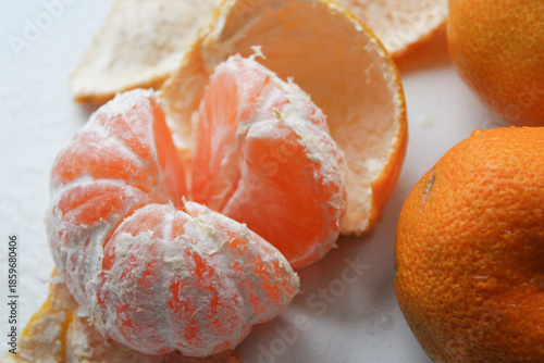 Billede på lærred Peeled tangerine revealing juicy orange segments with white pith visible among citrus fruits and peel on surface