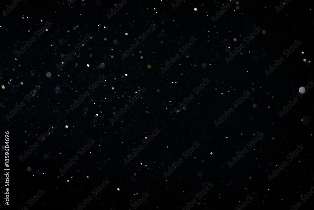 Fototapeta premium Tiny dust randomly flying in the smoky air, empty space template for objects advertisement. Dust particles of white powder in low light on empty dark black contrast background, close shot.