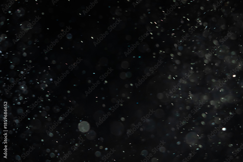 Obraz premium Soaring little pieces of dust floating in a ray of light on a black background. Twirling randomly as if blown by wind moving quickly through space. Each of them flying independently and dynamically.