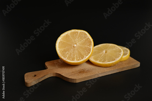 Freshly sliced organic lemons and a stainless steel kitchen knife on a wooden board. Minimalist culinary composition on a dark backdrop.