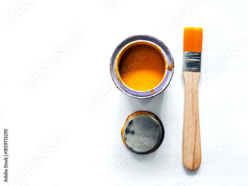 An open tin of bright yellow paint and paintbrush on a white wooden surface.