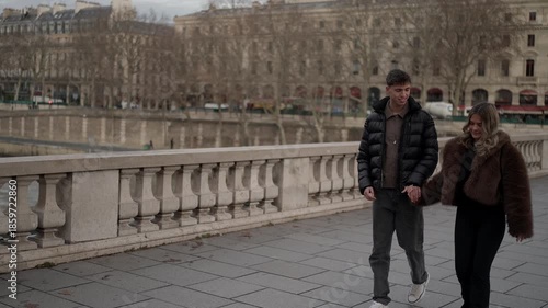 A couple walks hand-in-hand along the Seine River embankment in Paris France The clip captures a romantic stroll with cityscape views on a cloudy day showcasing love and travel in European.